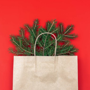 Kırmızı zemin üzerinde köknar dalları bulunan şenlikli Noel kompozisyonu. Kraft kağıdında çevre dostu ambalaj. Düzleştir, kopyala, taklit et, tebrik kartı