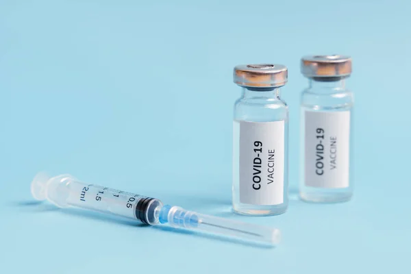 Vaccine and syringe injection against blue background. Coronavirus vaccine. COVID-19 immunization. Healthcare and medical concept. Copy space, front view.