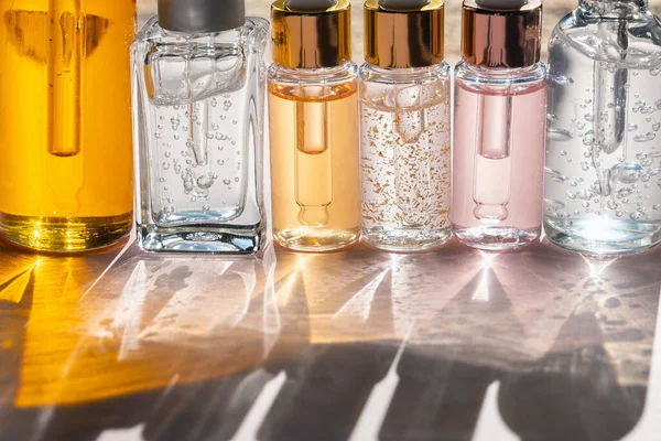 Farklı cam şişelerde güzellik serumu ya da yağ ya da güneş ışığında pastel pembe arka planda gölgeli losyon ürünleri. Güzellik kavramı, kozmetoloji, dermatoloji. Ön görünüm, kopyalama alanı, yakın plan