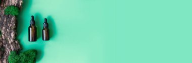 İki kahverengi serumun ya da yağlı camın pankartı ağaç kabuğu ve yosunların doğal yeşil arka planında pipetle şişeyi taklit eder. Doğal organik kozmetik kavramı. Düz yat, boşluğu kopyala