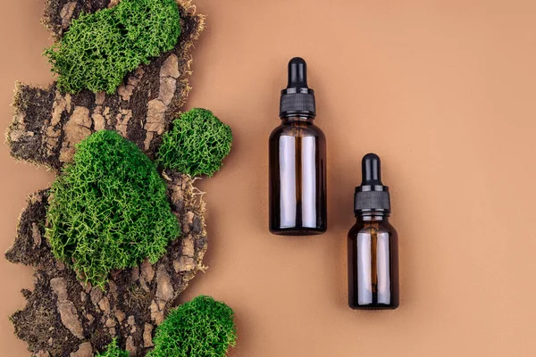 Bir çift kahverengi serum ya da yağ camı ağaç kabuğu ve yosunların doğal kahverengi arka planında pipeti olan şişeleri taklit eder..