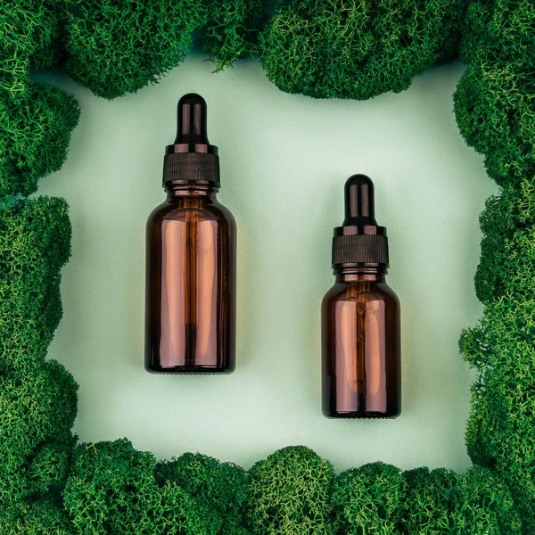 Two brown serum or oil glass mock up bottles with pipette over natural green background of moss.