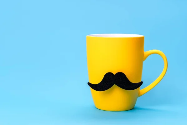 Yellow mug with a black mustache on blue background.