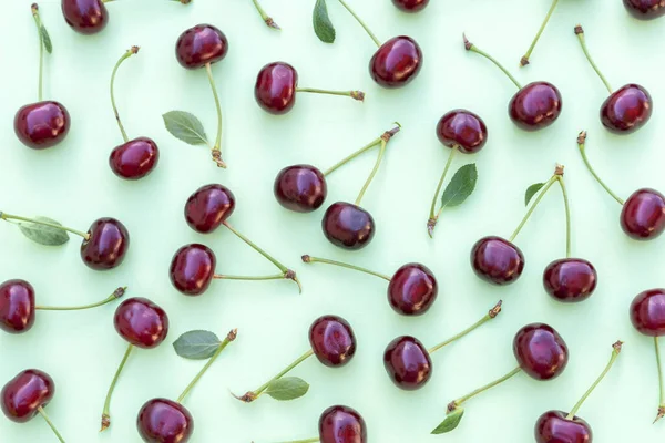 Cherry pattern. Flat lay of cherries and leaves on a soft green background. — Photo