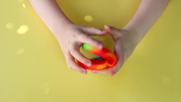 Close-up de uma criança mãos brincando com Popit na cor do arco-íris e forma do coração no fundo amarelo. — Vídeo de Stock