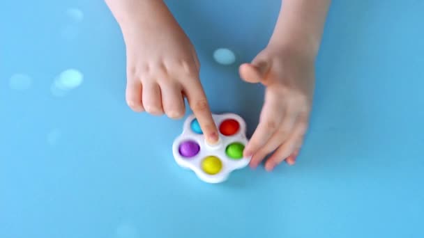 Вид сверху детской руки, играющей с Simple Dimple spinner на ярко-синем фоне. — стоковое видео