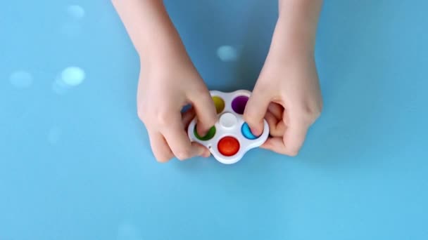 Vista superior de un niño manos jugando con Simple Dimple spinner sobre fondo azul brillante. — Vídeos de Stock