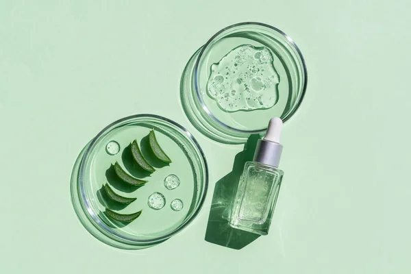 Düz bir kozmetik serumu ve parlak yeşil arka planda taze aloe vera yapraklı laboratuvar camları. Organik kozmetik ürünleri. Üst görünüm düzlüğü, kopyalama alanı. Kozmetik, SPA markalaşması, maket.