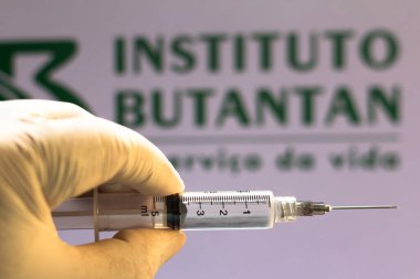 November 10, 2020, Brazil. In this photo illustration the medical syringe (coronavirus vaccine) is seen with Instituto Butantan company logo displayed on a screen in the background clipart