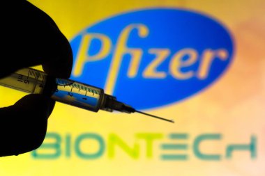 11 Kasım 2020, Brezilya. Bu resimde tıbbi şırınga (coronavirus aşısı), Pfizer ve BioNTech SE firmalarının logosu arka planda bir ekranda sergilenmektedir.