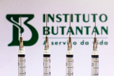 December 4, 2020, Brazil. In this photo illustration various medical syringes is seen with Instituto Butantan company logo displayed on a screen in the background clipart