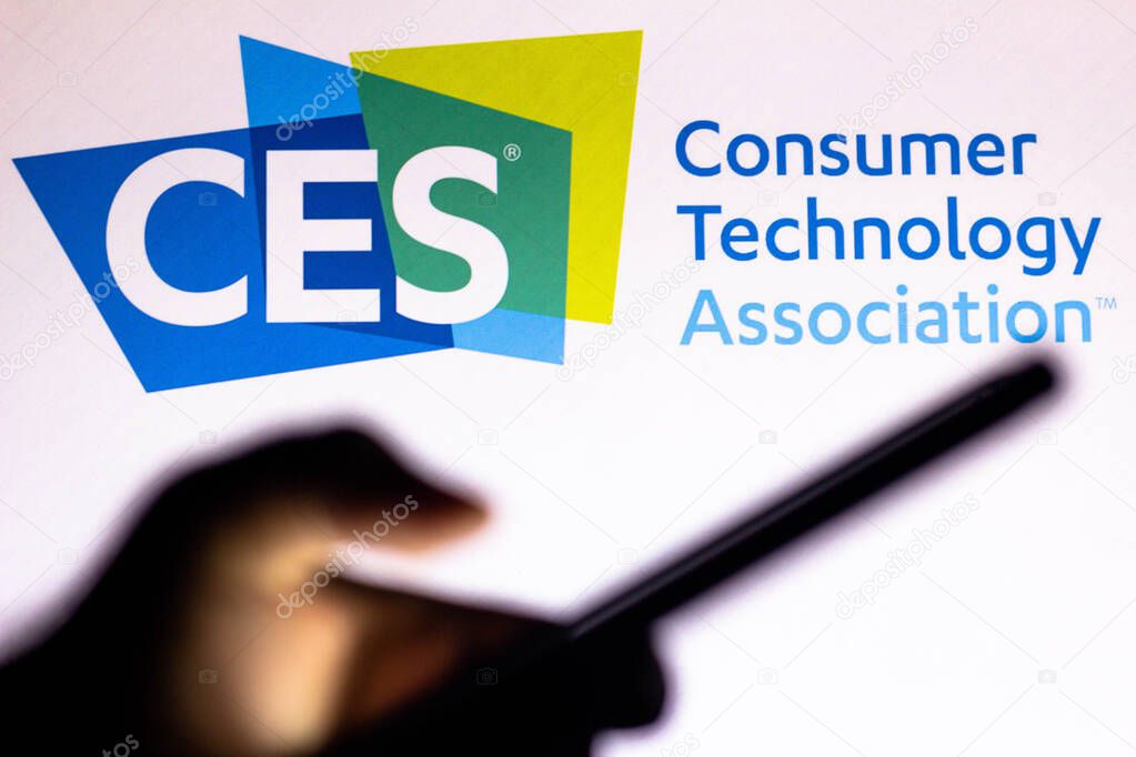 January 20, 2021, Brazil. In this photo illustration the Consumer Electronics Show (CES) logo seen in the background of a silhouette hand holding a mobile phone