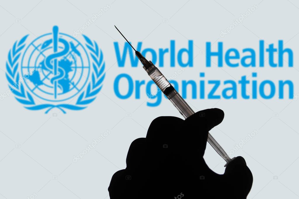 April 1, 2021, Brazil. In this photo illustration the medical syringe is seen with World Health Organization (WHO) company logo displayed on a screen in the background