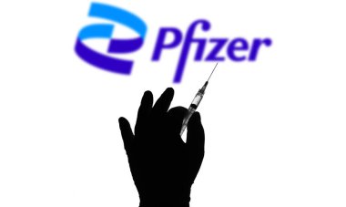 12 Nisan 2021, Brezilya. Bu resimde tıbbi şırınga ve Pfizer şirketinin logosu arka planda bir ekranda görülüyor.