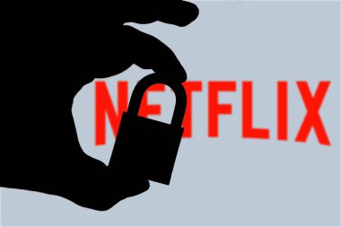 Bu resimde bir adam asma kilit tutuyor ve arka planda bilgisayar ekranında Netflix logosu var. Çevrimiçi veri koruması - ihlal kavramı. İnternet gizlilik sorunları