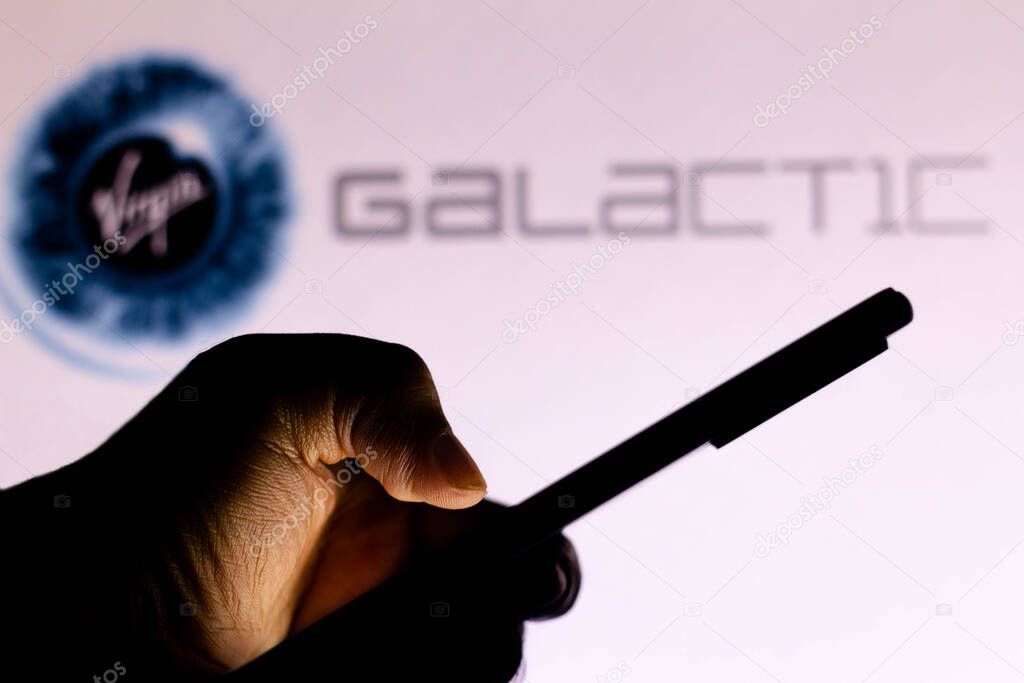 May 19, 2021, Brazil. In this photo illustration the Virgin Galactic logo seen in the background of a silhouette hand holding a mobile phone