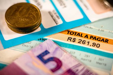 21 Haziran 2021, Brezilya. Bu illüstrasyonda, yan tarafında Brezilya 'nın gerçek paraları ve beş gerçek banknotuyla ödenecek toplam miktarı gösteren bir elektrik faturası var.