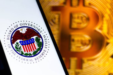 7 Ağustos 2021, Brezilya. Bu resimde Federal Rezerv Yönetim Kurulu logosu bir akıllı telefonda sergileniyor. Arka planda, bir bitcoin şifreleme birimi görüntülenir