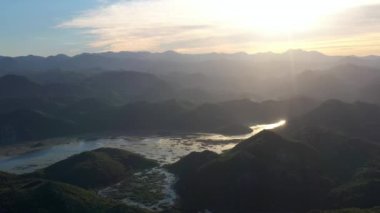 Karadağ 'ın gün batımında Skadar Gölü' nün sularındaki yeşil dağların panoramik manzarası