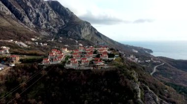 Sonbaharda günbatımında yüksek dağ sıralarında turuncu çatıları, kahverengi çalıları ve ağaçları olan villalar.