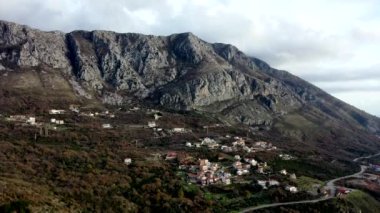 Beyaz evler ve villalar, yüksek dağ sıralarında turuncu çatılar, günbatımında güz boyunca kahverengi çalılar ve ağaçlar.