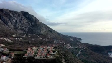 Sonbaharda günbatımında, yüksek dağ sıralarında turuncu çatıları, kahverengi çalıları ve ağaçları olan küçük köyün üzerinden uç.