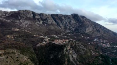 Sonbaharda günbatımında yüksek dağlarda turuncu çatılar, kahverengi çalılar ve ağaçlarla çevrili.