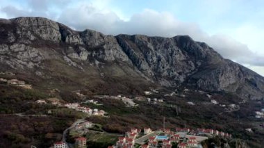 Sonbaharda günbatımında yüksek dağ sıralarında turuncu çatıları, kahverengi çalıları ve ağaçları olan küçük bir köy.