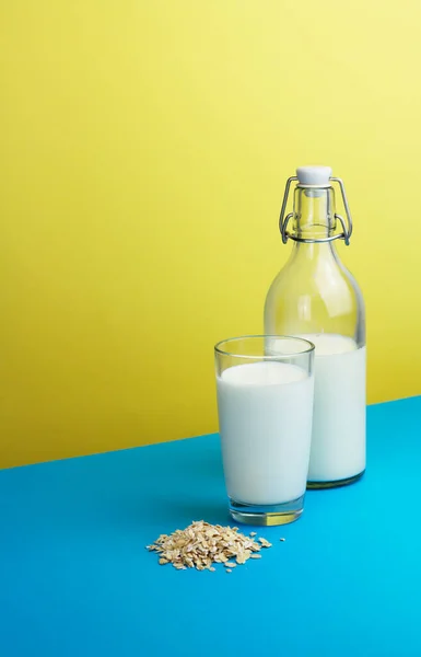 Ovesné mléko ve sklenici a láhev na trendy žluté modré pozadí — Stock fotografie