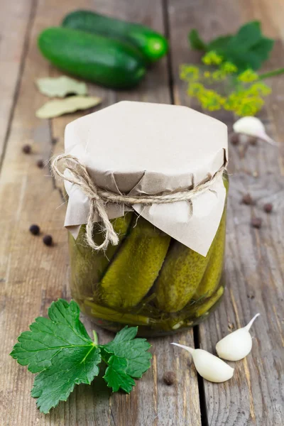 Pickled cucumbers in a glass jar on wooden background. Close up