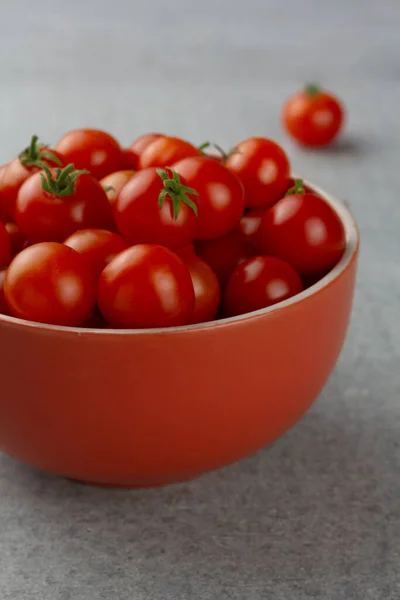 Kirschtomaten in einer roten Schüssel auf grauem Hintergrund — Stockfoto