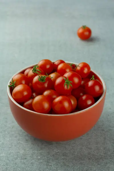 Kirschtomaten in einer roten Schüssel auf grauem Hintergrund. Selektiver Fokus — Stockfoto