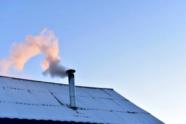 Iron chimney with smoke on the roof in winter