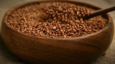 Yemek videosu yavaş çekimde çekildi. Bir adam ahşap bir tabağa çiğ karabuğday döker kırsal bir masada tahta bir kaşıkla. Yüksek çözünürlüklü çekim.