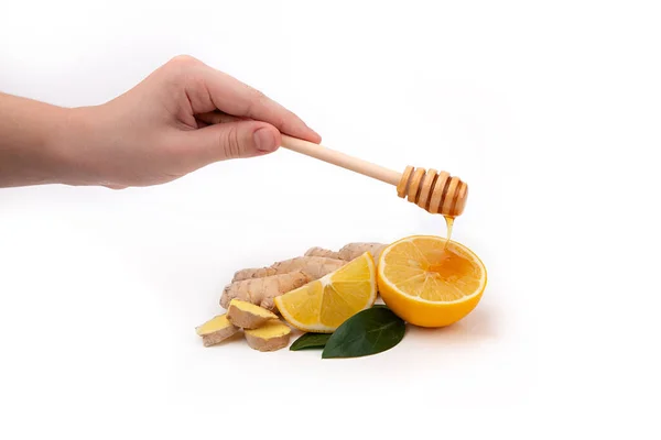 A woman\'s hand holds a wooden honey spoon and pours honey over a lemon. Isolated pieces of ginger and lemon with honey.