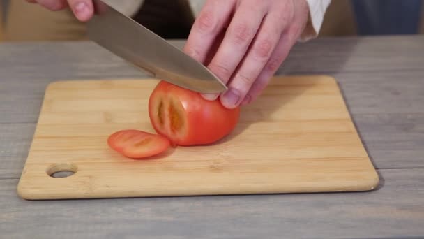 Чоловічий шеф-кухар нарізає помідор кухонним ножем на дерев'яний стіл — стокове відео