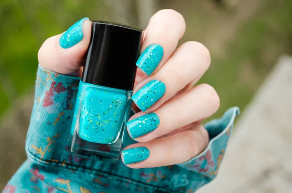Bright turquoise Nail art manicure. Holiday style nails with neon glitter. Woman holds Bottle of Nail Polish. Sumer autumn winter fashion trands
