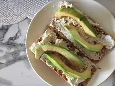 Avokado tostu, krem peynirli, tabakta tuz ve biberli ve beyaz mermer arka planda. Sağlıklı kahvaltı ya da atıştırmalık.