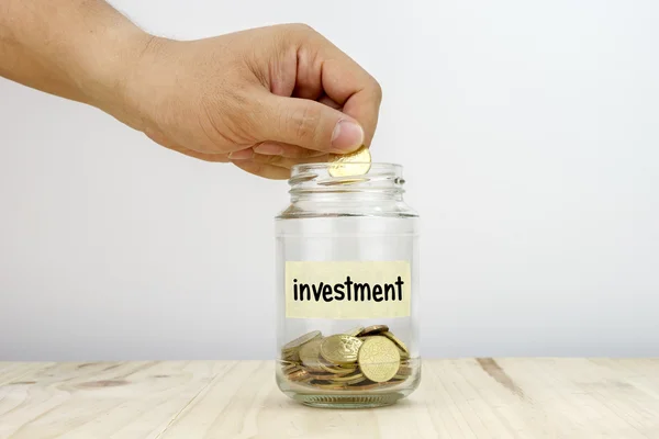 Hand putting a coin into a glass jar — Stock Photo, Image