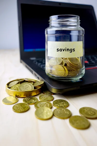 Garrafa de vidro com moedas de ouro e laptop na mesa — Fotografia de Stock