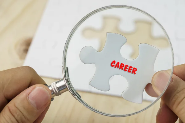 Hands with magnifying glass and piece of jigsaw puzzle — Stock Photo, Image