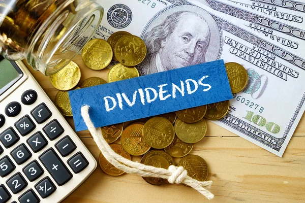 DIVIDENDS sanoja, sata dollaria seteleitä, kultakolikoita ja laskin puinen tausta . — kuvapankkivalokuva