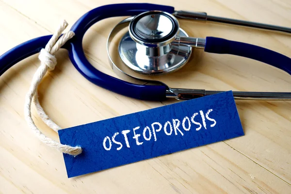 OSTEOPEROSIS mot inscrit sur l'étiquette et stéthoscope sur fond en bois . — Photo