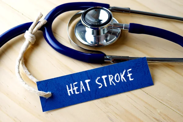 Слово HEAT STROKE написано на этикетке и стетоскоп на деревянном фоне . — стоковое фото