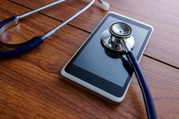 Smartphone siendo diagnosticado con un estetoscopio sobre fondo de madera . — Foto de Stock
