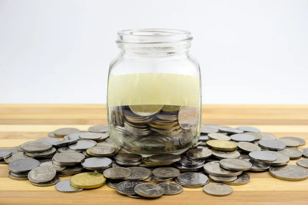 Coins in glass container on wooden surface — Stock Photo, Image