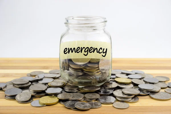 Coins in glass container on wooden surface — Stock Photo, Image