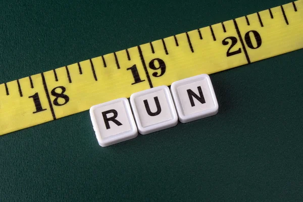 Arrangement of alphabet blocks of word RUN with yellow tape measure — Stockfoto