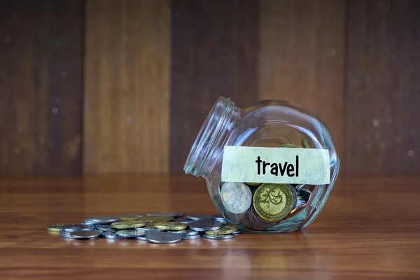 Münzen und Glasbehälter mit Reiseetikett auf Holzgrund — Stockfoto