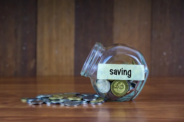 Monedas y recipiente de vidrio con etiqueta de ahorro sobre fondo de madera — Foto de Stock